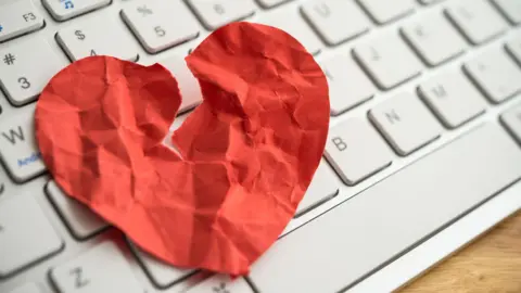 Getty Images A paper heart which is torn and crumpled on top of a white computer keyboard.