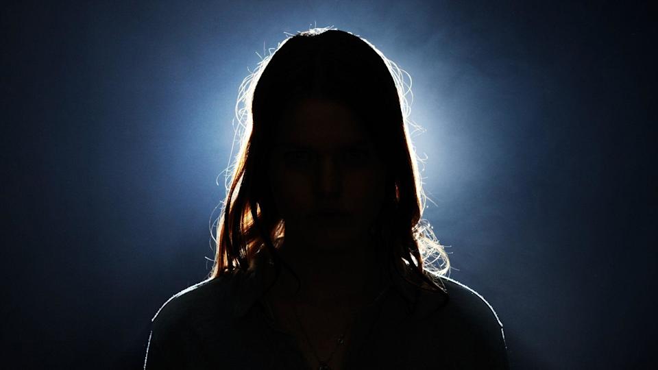 A young woman's head can be seen in silhouette, with a bright light and dark background behind her.
