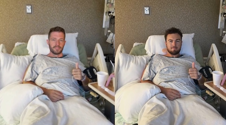 Man in hospital gown giving thumbs up from hospital bed.